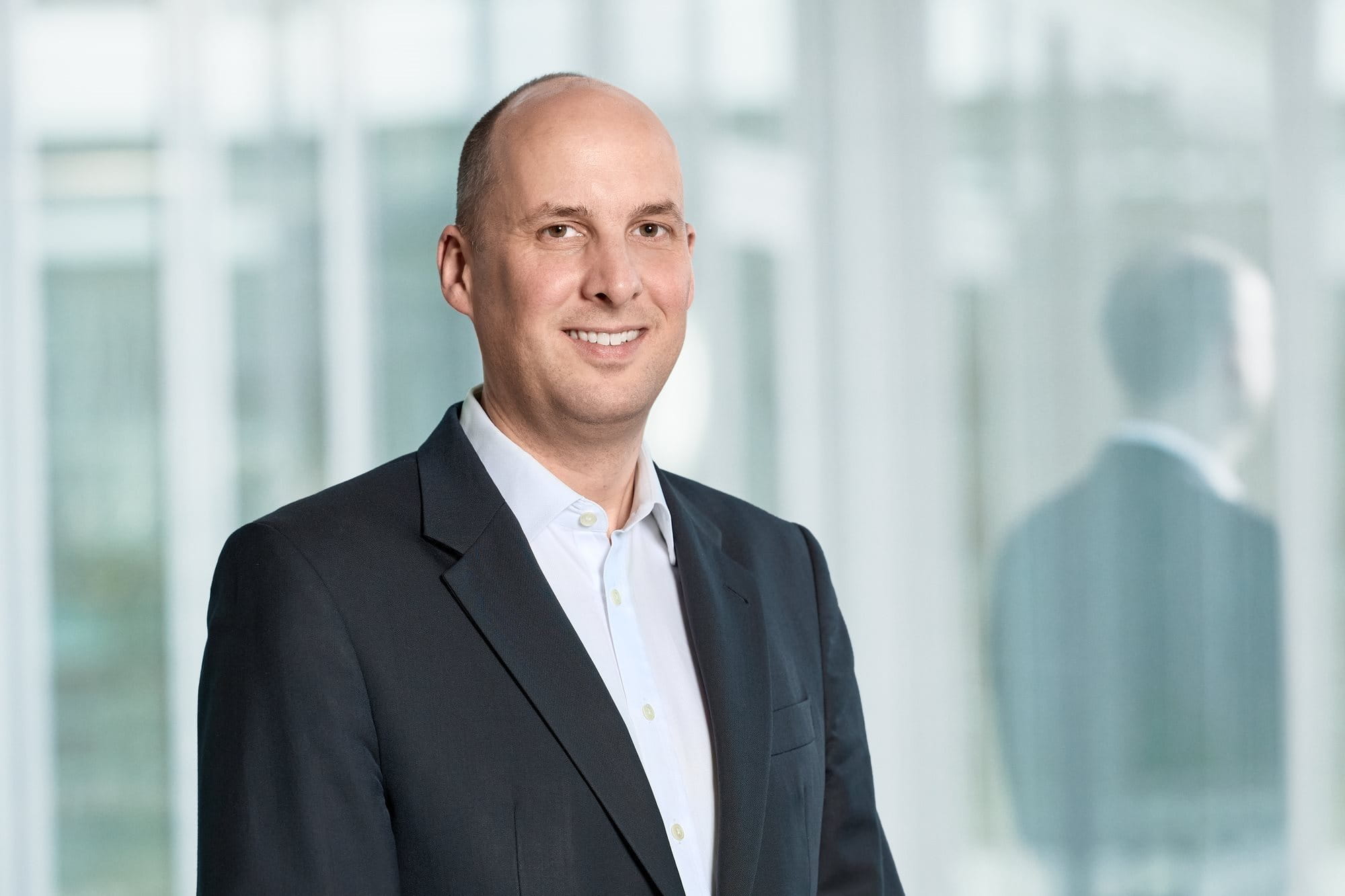 Christopher Sheldon Beiersdorf Investor Relations, Person in a suit smiling in a bright office setting.