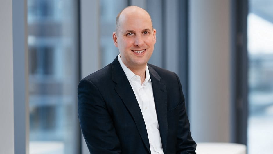 Christopher Sheldon Beiersdorf Investor Relations, Person in a suit smiling in a bright office setting.